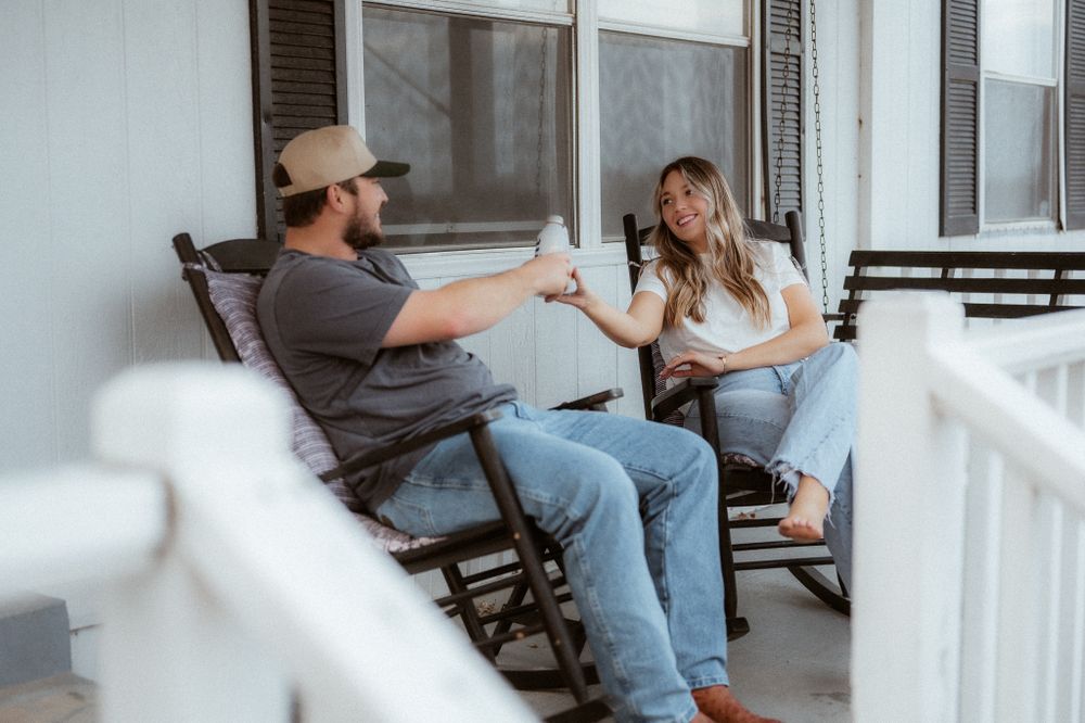 Couple sharing drinks while relaxing in rocking chairs on front porch.