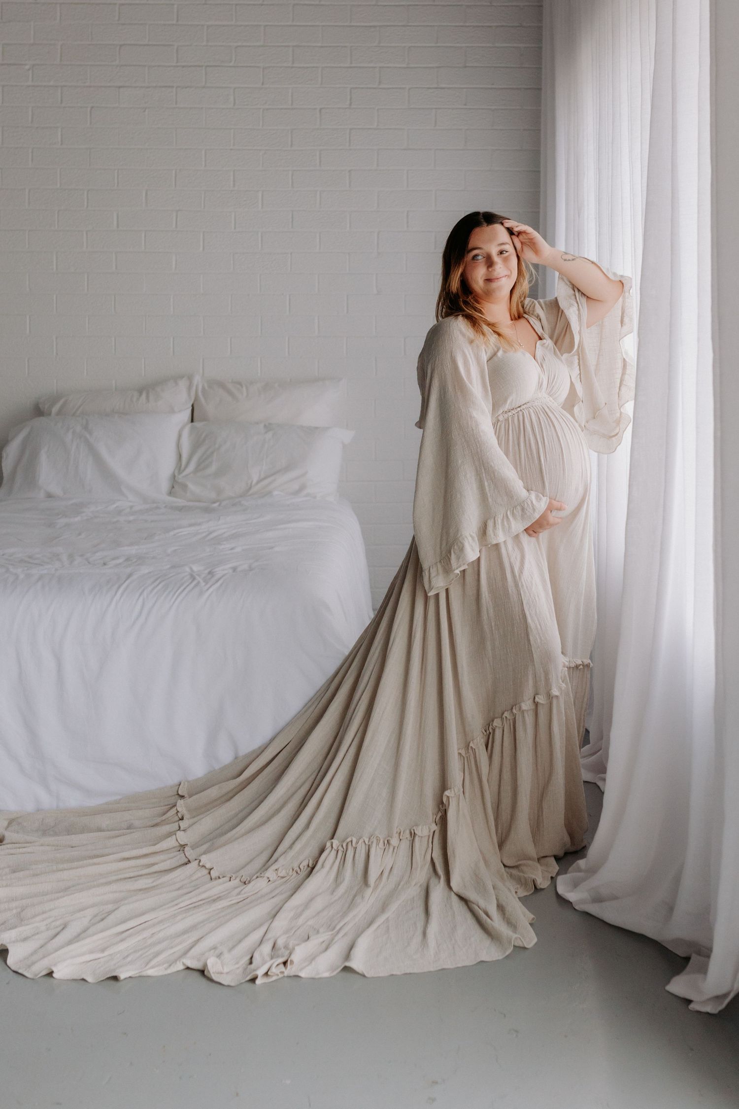Elegant flowy beige maternity gown with long bell sleeves, empire waist, and dramatic cathedral-length train.