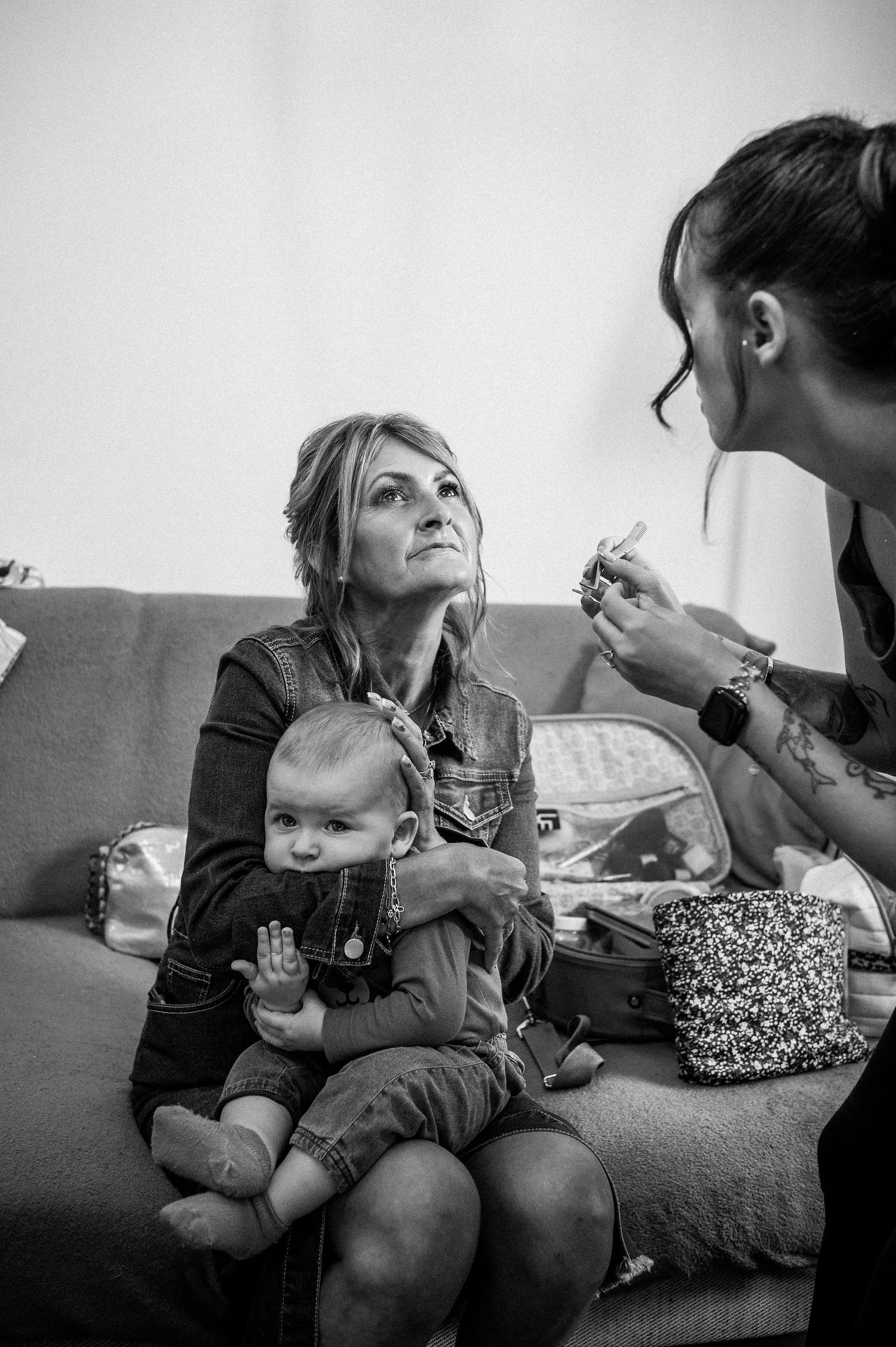 Une grand-mère tenant un bébé sur ses genoux, pendant qu’une jeune femme applique du maquillage, illustrant la transmission et la vie