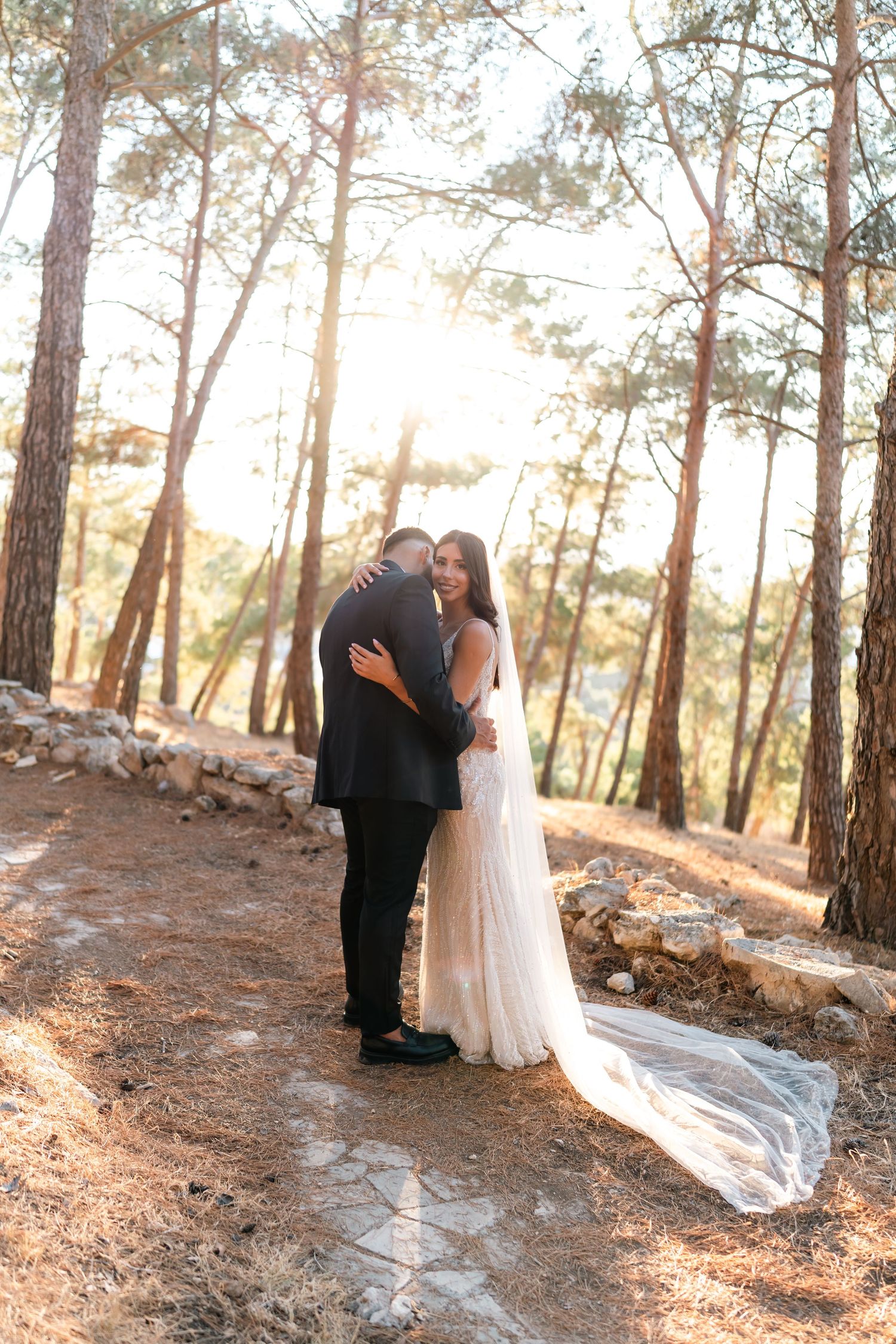 Intimate wedding couple portrait on forest path surrounded by tall pine trees.