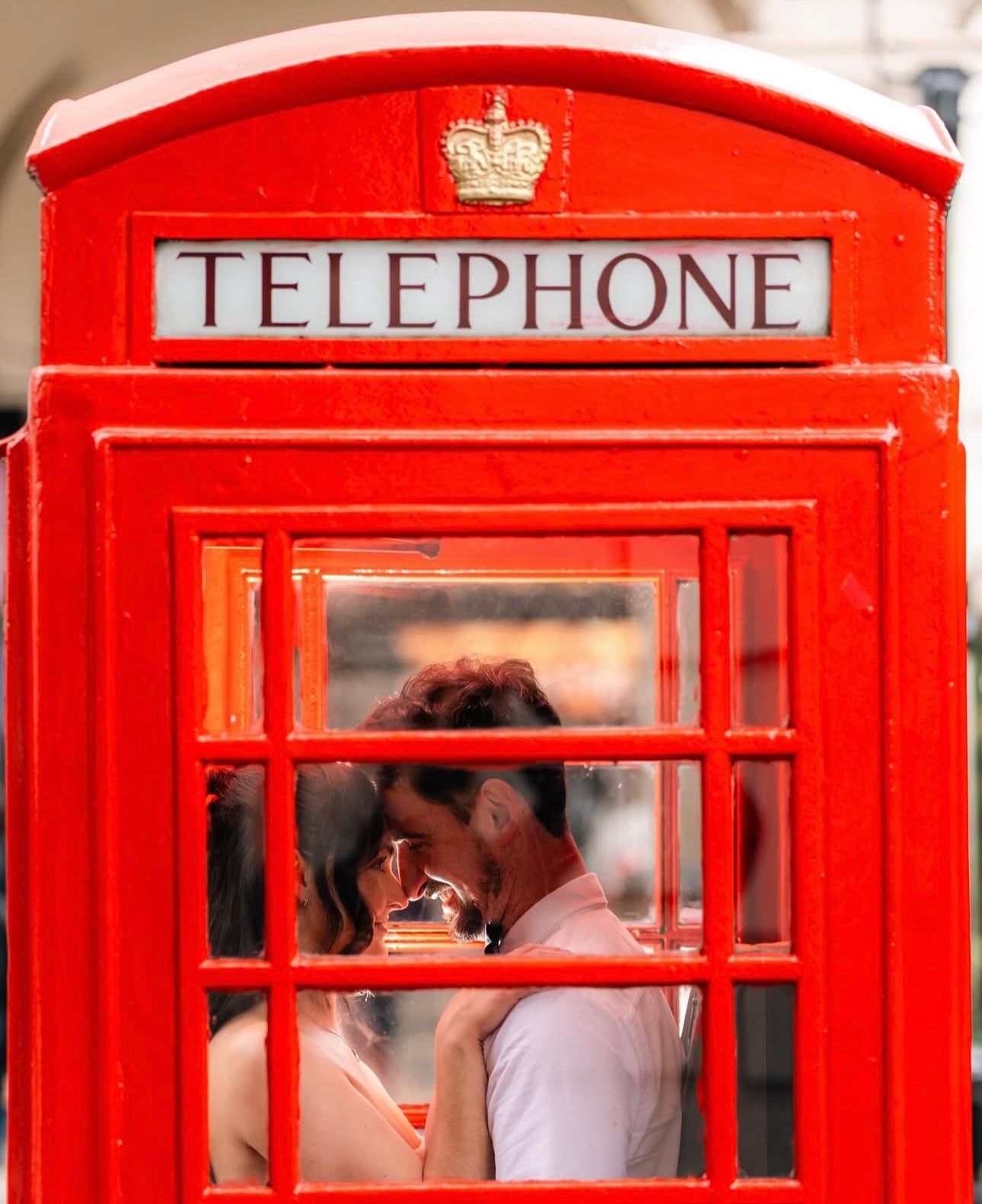 A romantic moment captured through a classic red British telephone booth window.