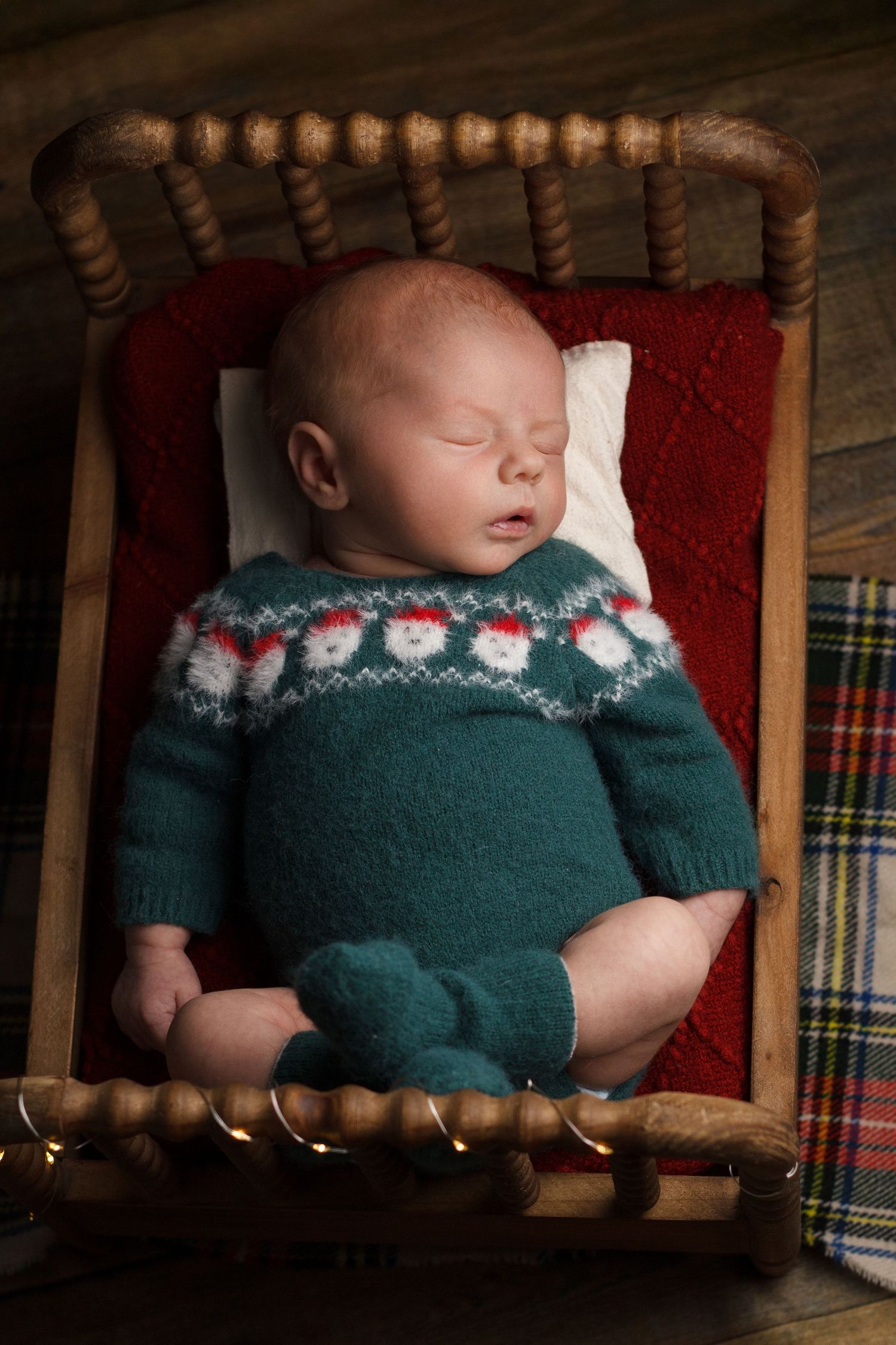 Newborn baby sleeping in a small wooden bed wearing a green knit sweater during a cozy newborn photography session.