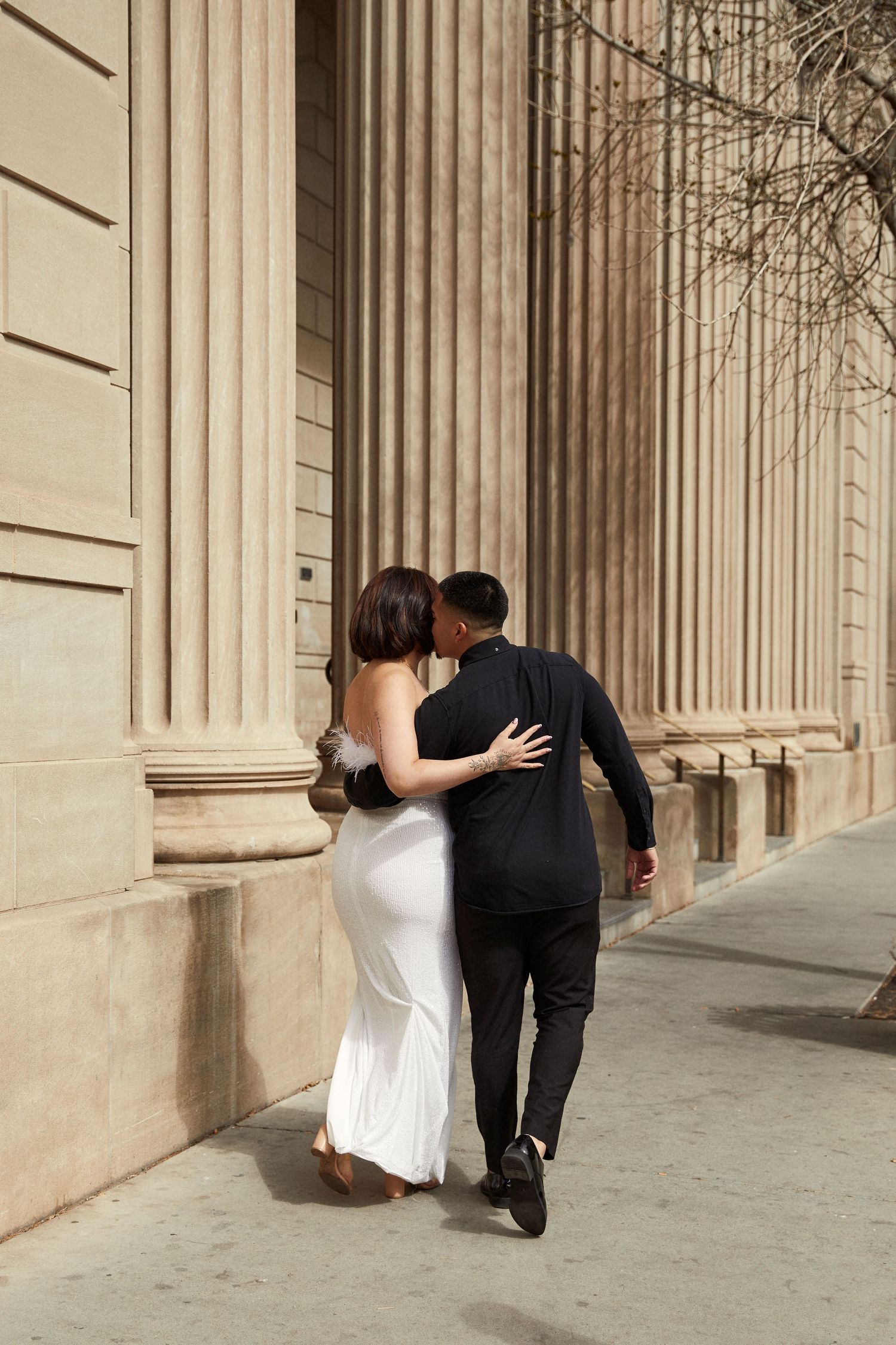 Romantic couple in wedding attire share intimate moments against classical stone columns.