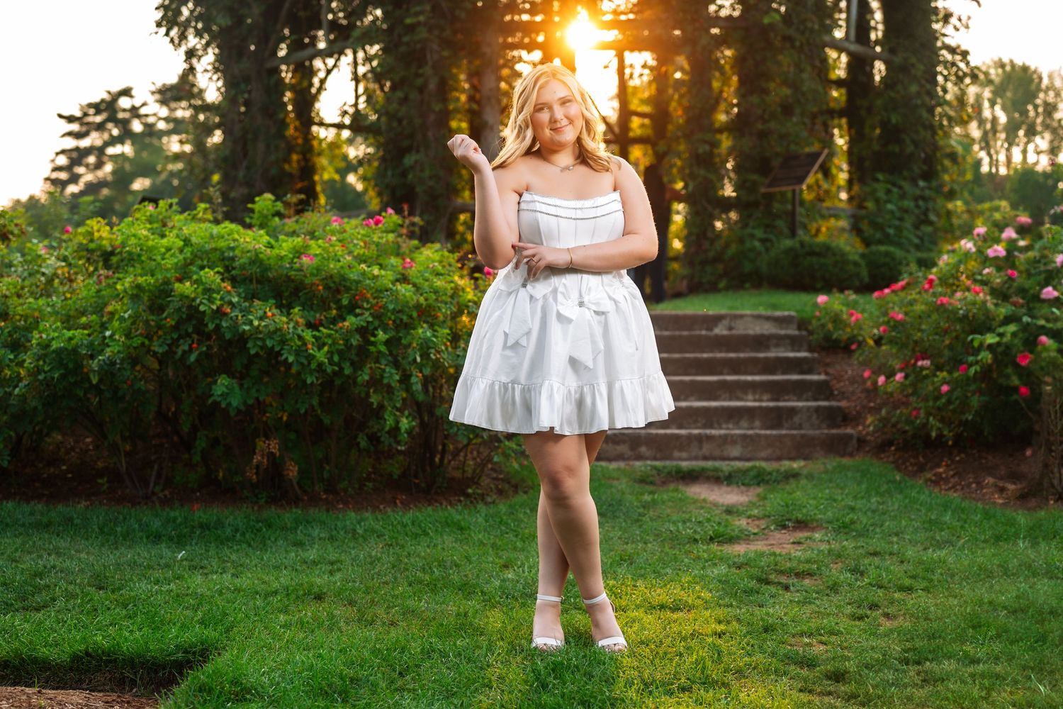 White dress twirling against sunset backdrop with green garden steps in background.
