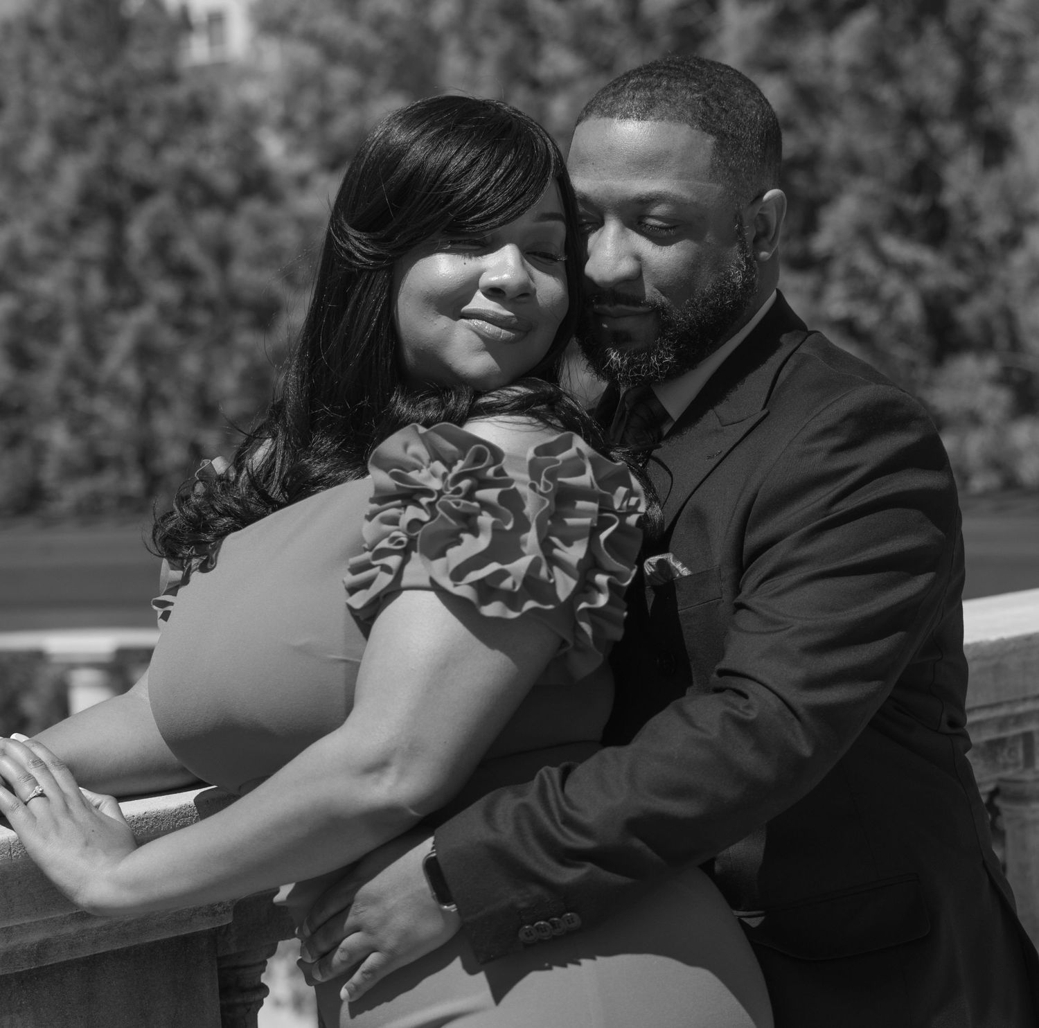 A romantic black and white portrait of a couple embracing outdoors, with soft focus and natural lighting.