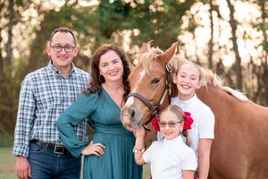 A family poses together with their brown horse in a wooded setting during golden hour.