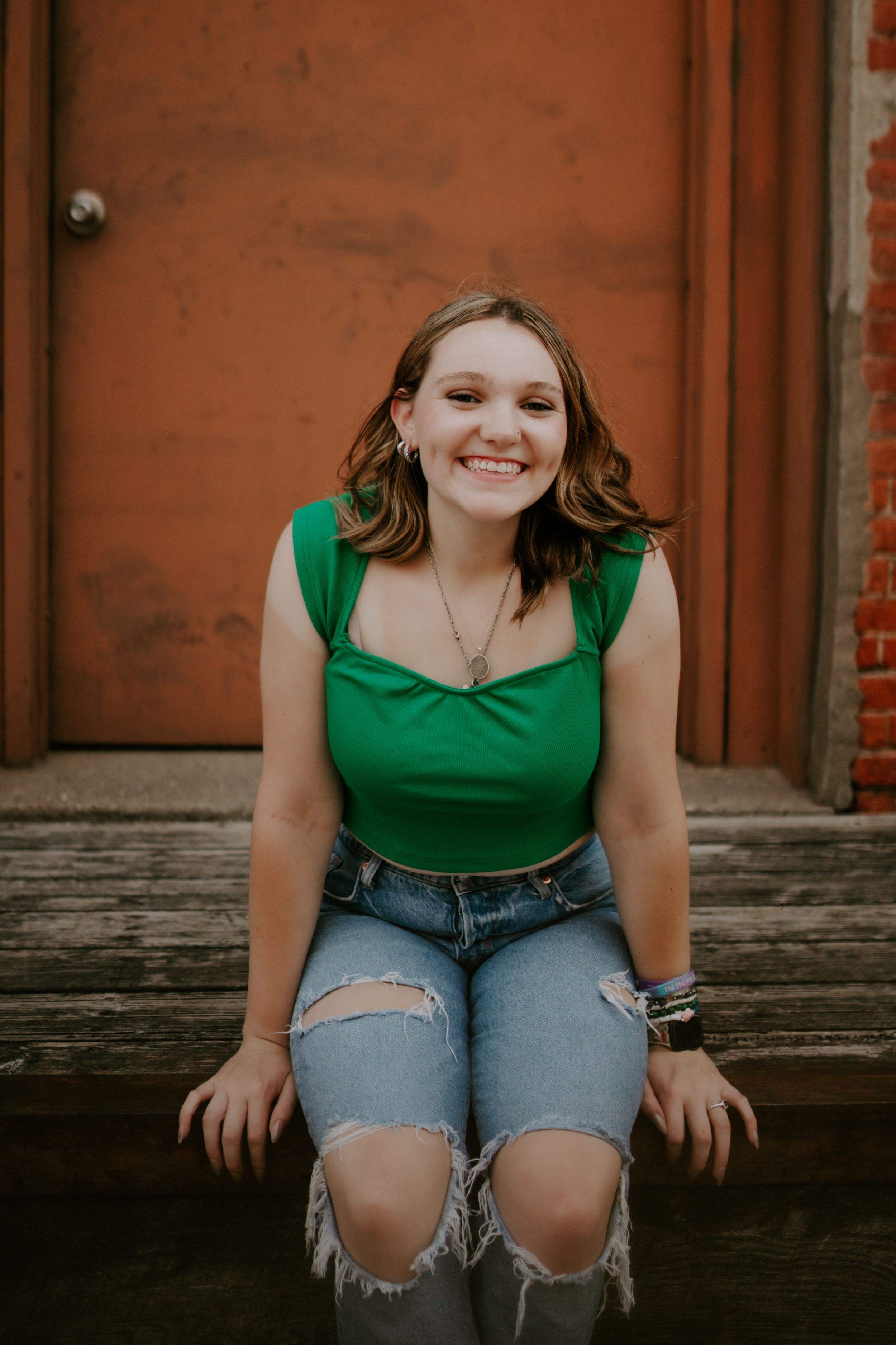 Casual portrait session on rustic wooden bench with green top and distressed jeans.