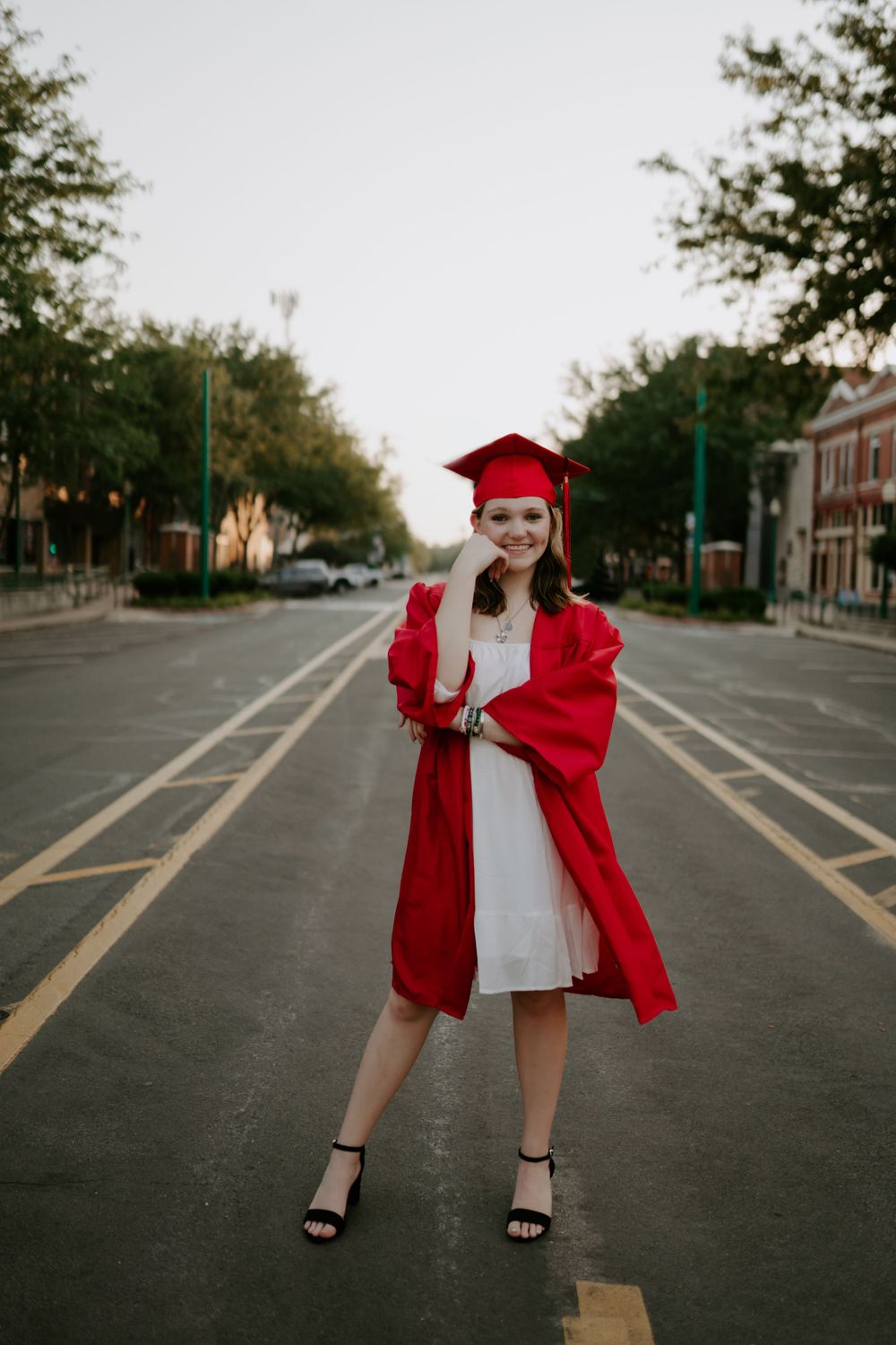 Playful graduation photos in a red cap and gown taken in an empty parking lot.
