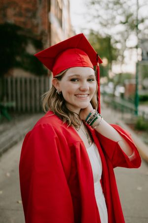 Candid graduation portraits in traditional red cap and gown against brick building backdrop.