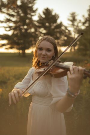 Ethereal outdoor violin playing sequence in flowing white dress at golden hour.