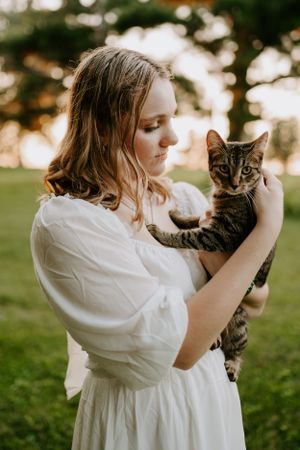 Sweet moments captured holding and playing with a tabby kitten in white dress outdoors.