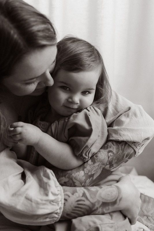 A tender black and white portrait capturing an intimate bonding moment between parent and child lounging on floral bedding.