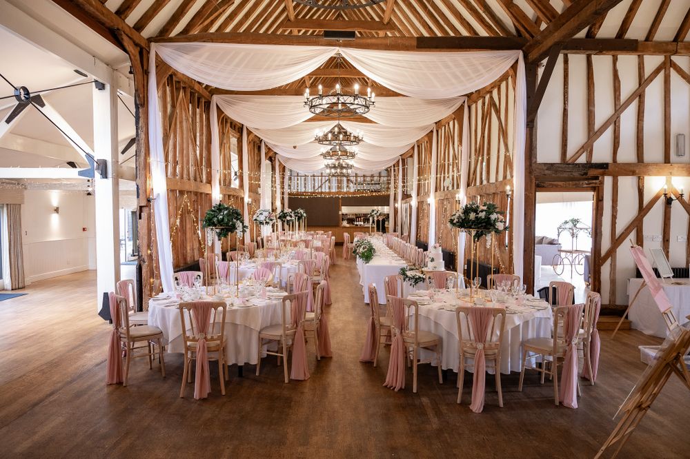 Elegant barn wedding reception venue with exposed wooden beams and white draping decorated with round tables and chairs.
