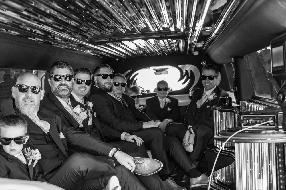 A group wearing sunglasses sits in a limousine interior with vinyl record storage visible.