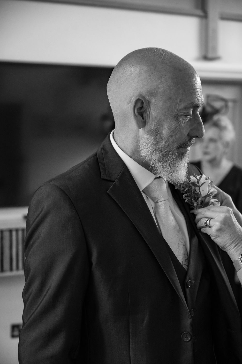 A person wearing a formal black suit and tie with a white boutonniere in black and white photo.