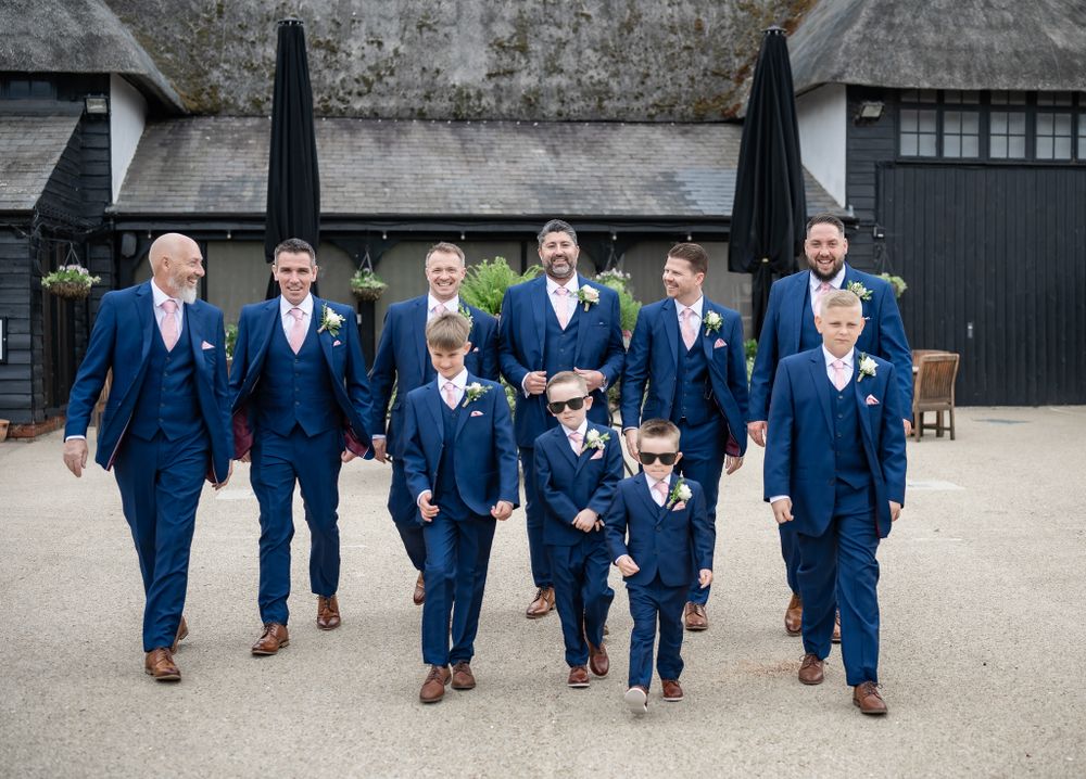 Groomsmen and children in matching navy blue suits walk together in a courtyard.