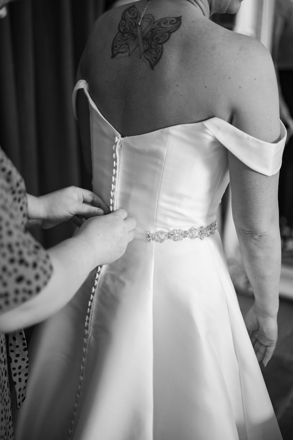 A white wedding dress being laced up, showing a butterfly tattoo on the wearer's back.