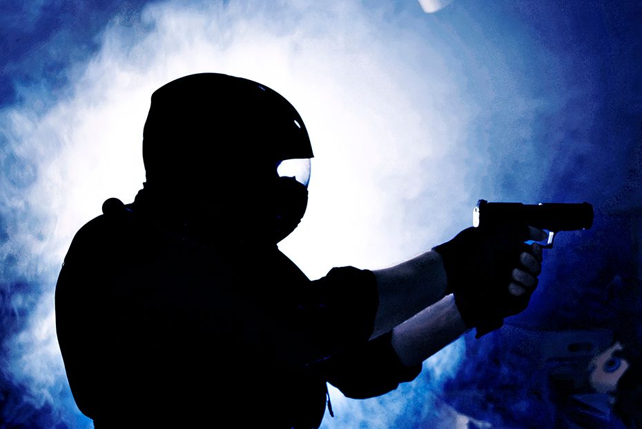 Silhouetted figure in tactical gear holding a handgun against dramatic blue moonlit sky.