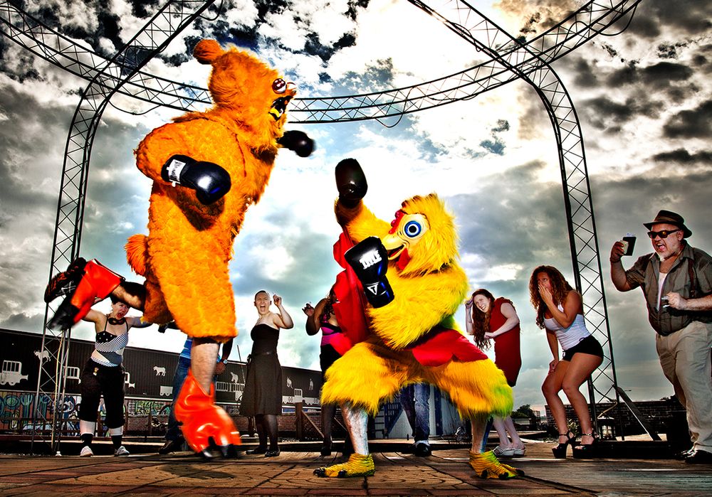 Costumed performers dancing energetically on an outdoor stage during a festival under dramatic cloudy skies, dressed as chickens