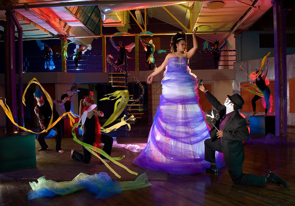 Performers in colorful costumes dance with ribbons around a glowing purple LED dress at a nighttime event. (Hilton New York)