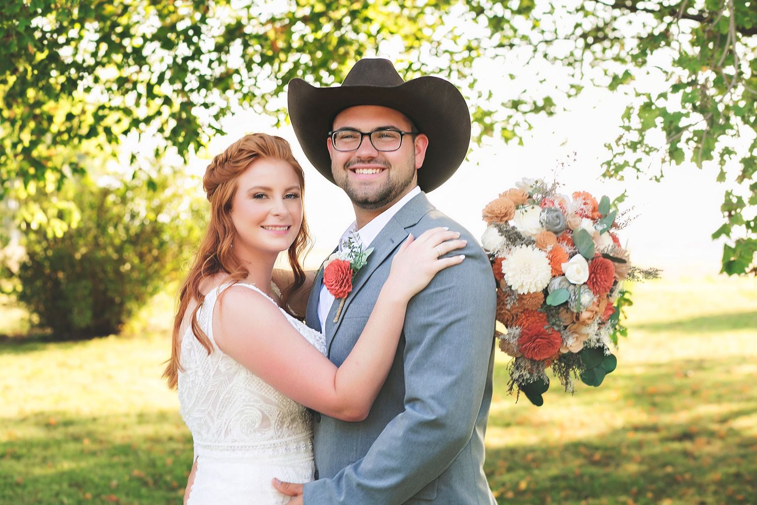 Wedding couple kisses next to white fence while holding elegant red and white bouquet.