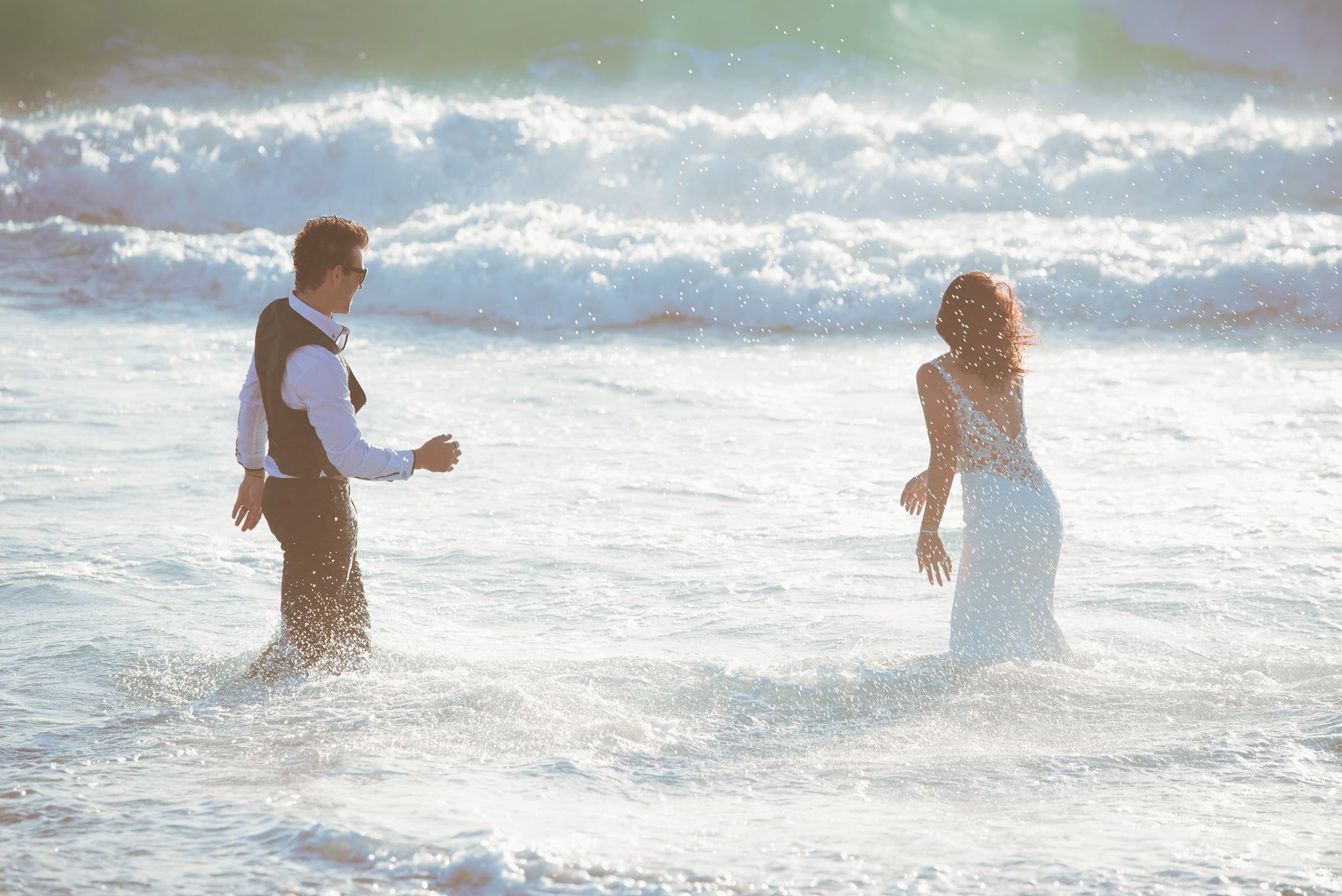 Couple wading through ocean waves during beach photoshoot.