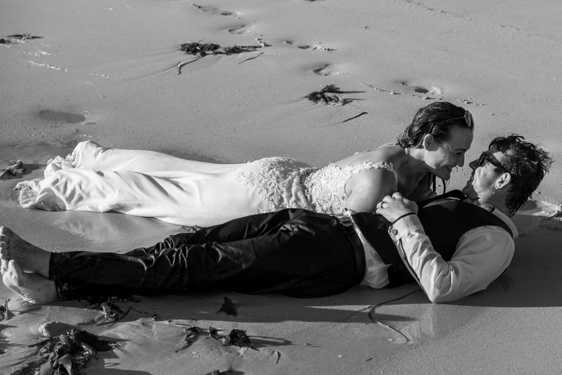 A romantic black and white photo of a couple lying together on a beach.