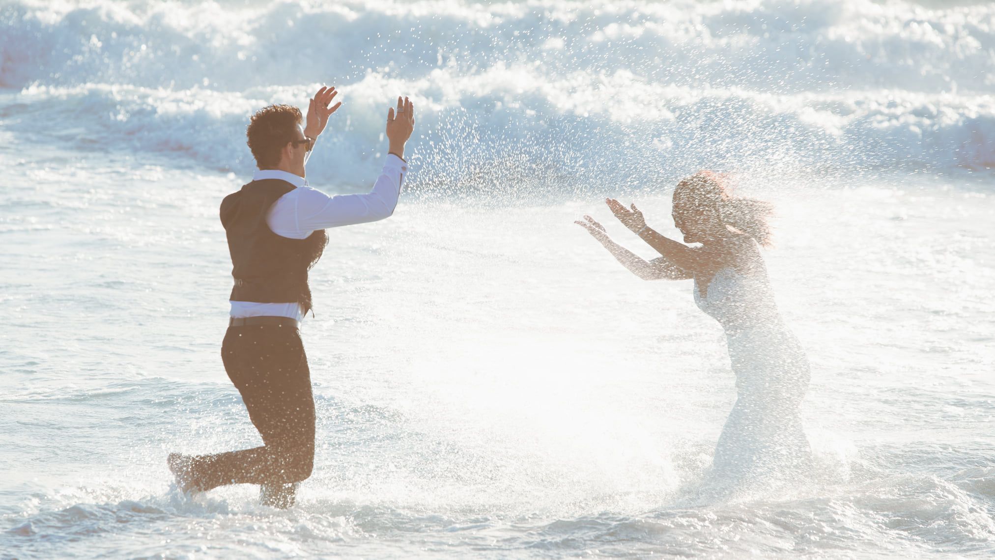 Two people playing and splashing in ocean waves at sunset.