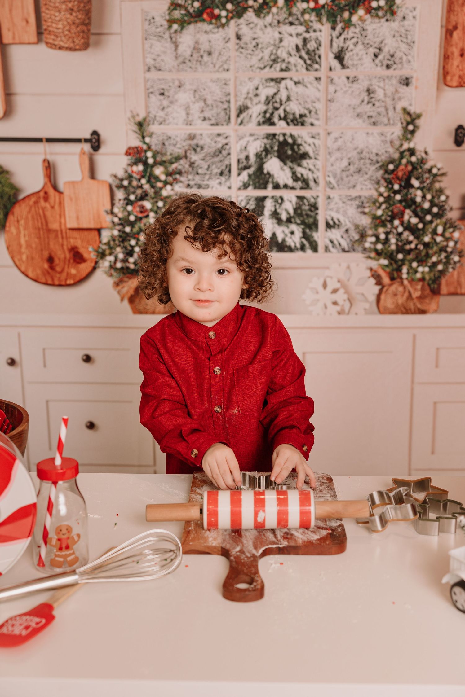 A small figure in a red shirt works on holiday baking with cookie cutters on a white counter.