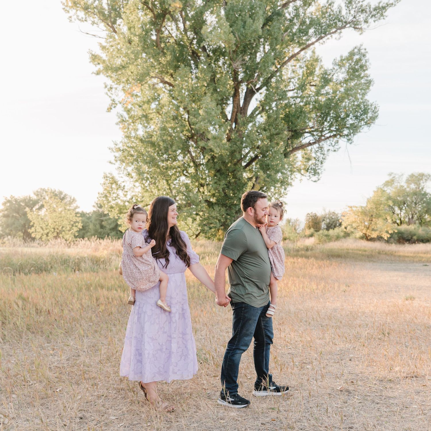 Family playing together in a golden field at sunset with tall trees in the background.