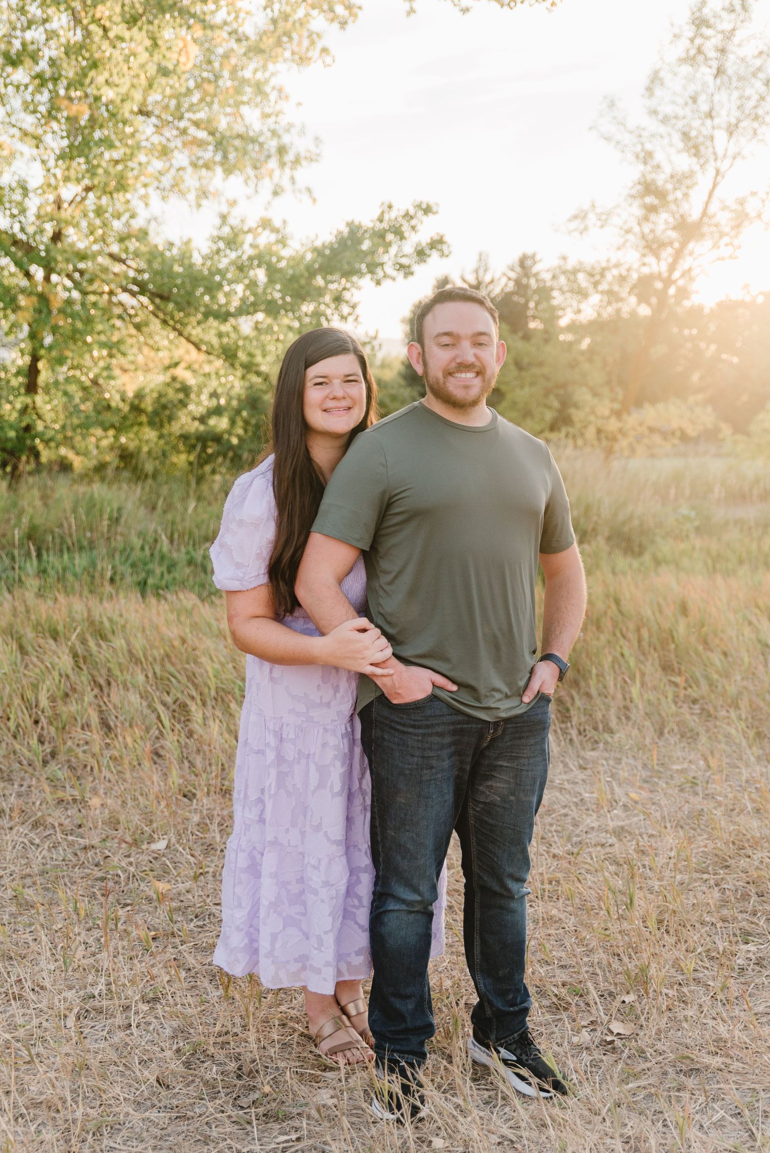 Couple posing in casual attire against natural golden field backdrop at sunset.