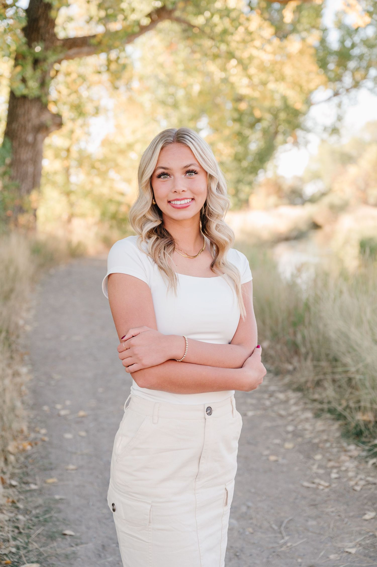 Portrait of woman in white outfit smiling on nature path during golden hour.