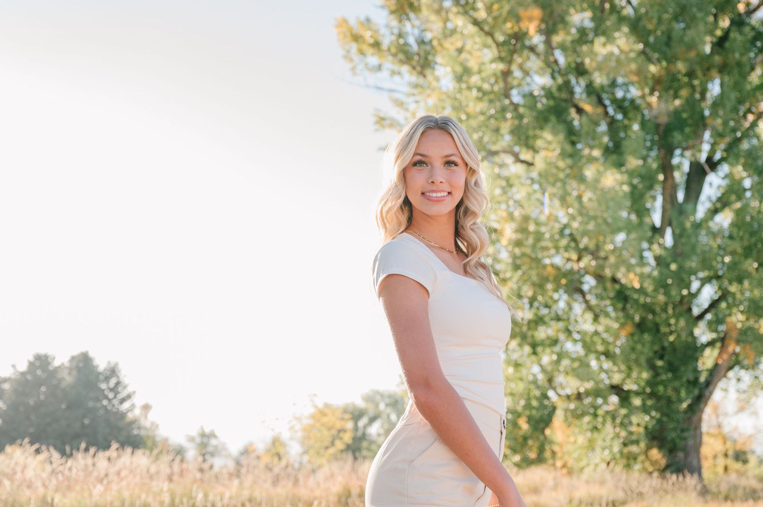 White sundress photo shoot in a golden field with tall trees at sunset.