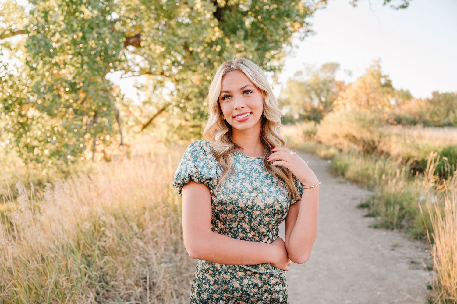 Woman wearing floral dress poses on nature trail during golden hour.