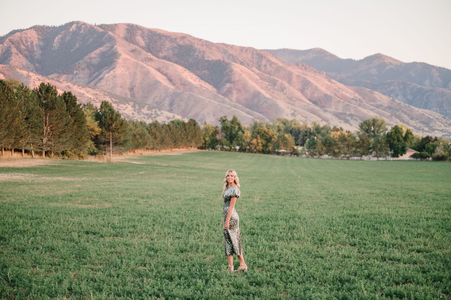 Distant figure stands in green field with mountain backdrop at sunset.
