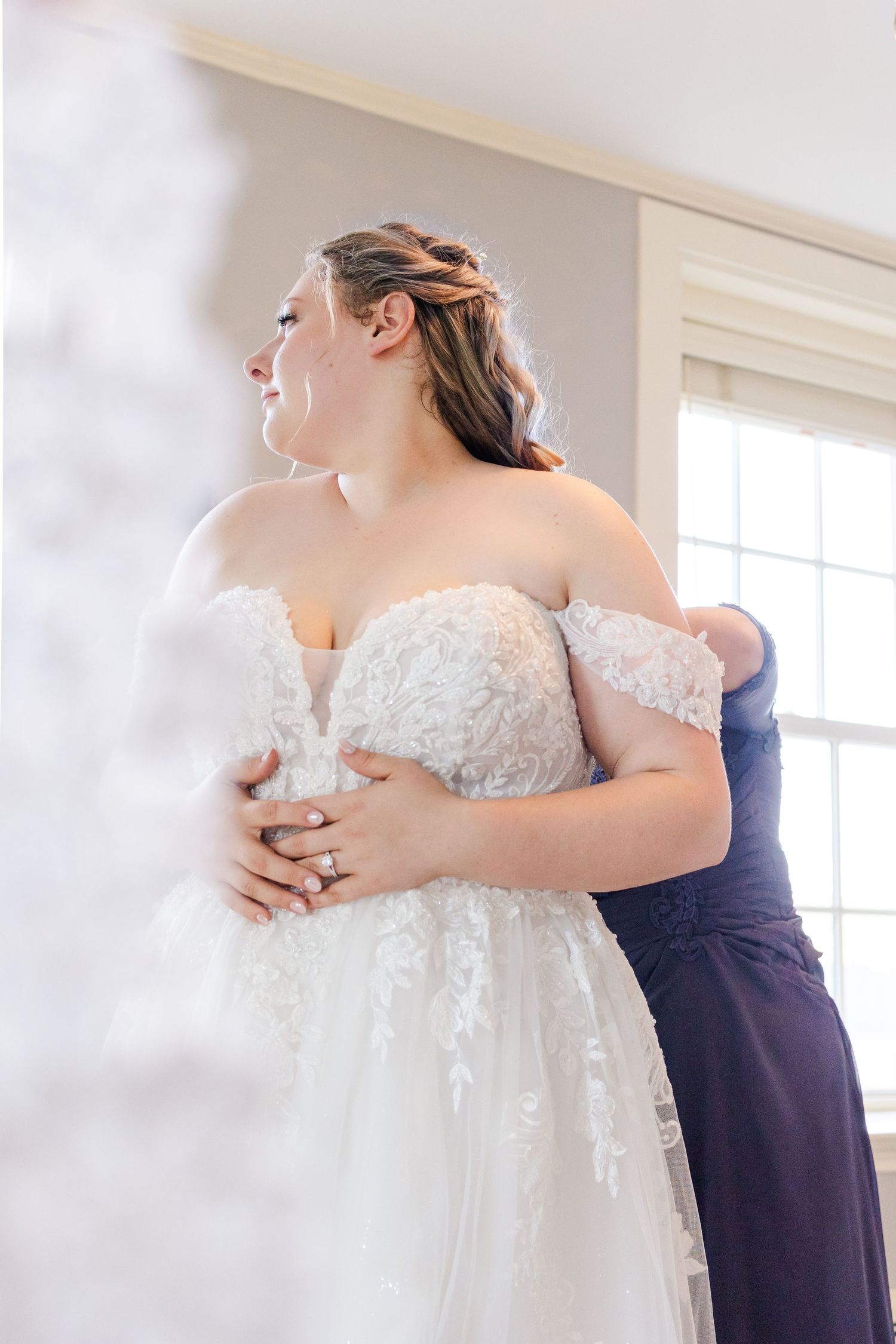 Fitting a beautiful white lace wedding gown with off-shoulder details.