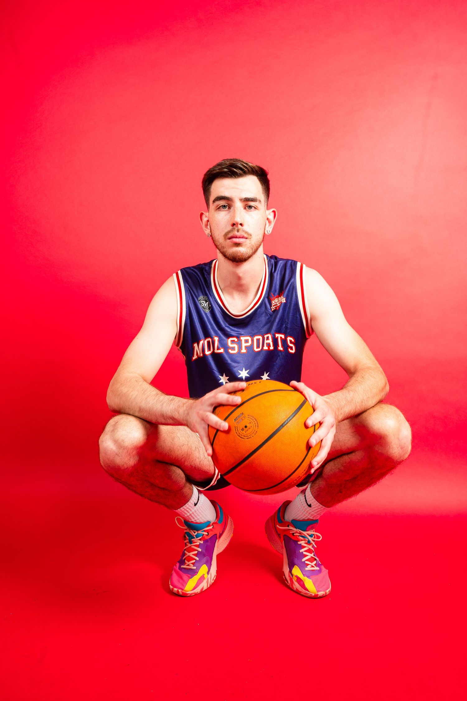 Basketball player in blue jersey poses with ball against red background.