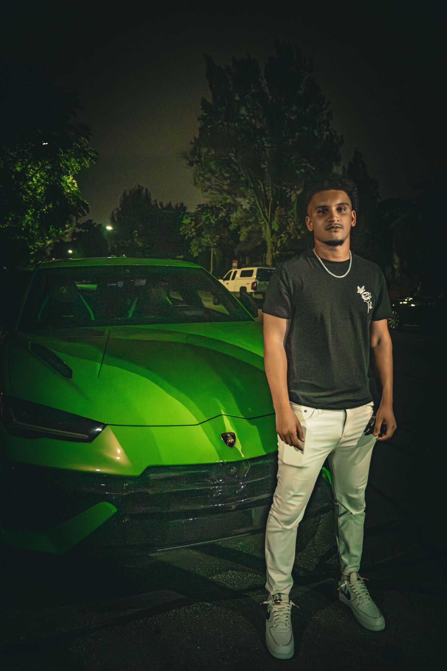 Nighttime portrait in front of bright green sports car wearing casual streetwear.