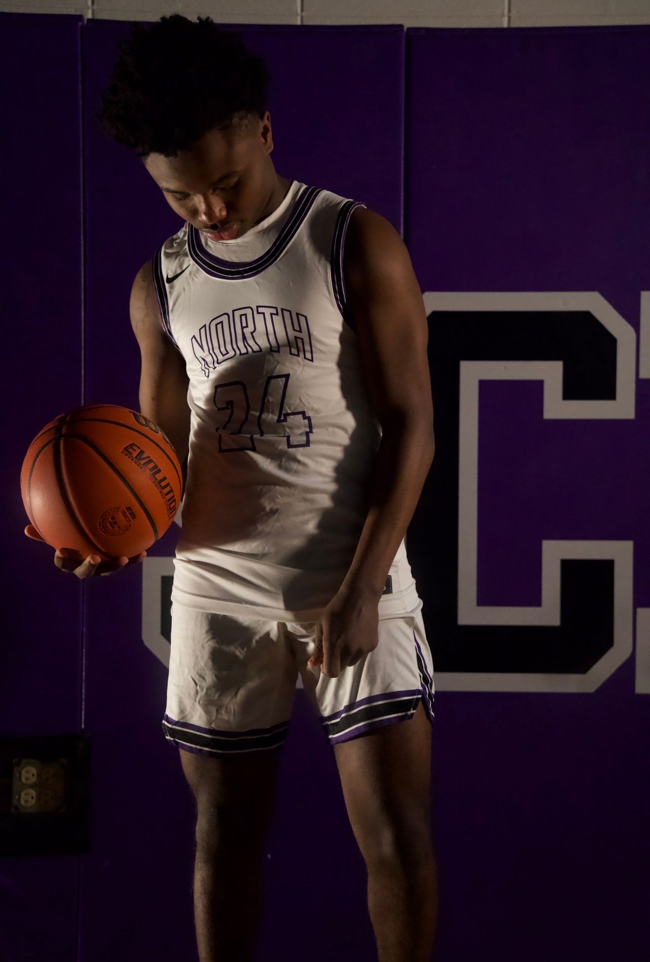 Basketball player in white North jersey holding ball in dramatic lighting.