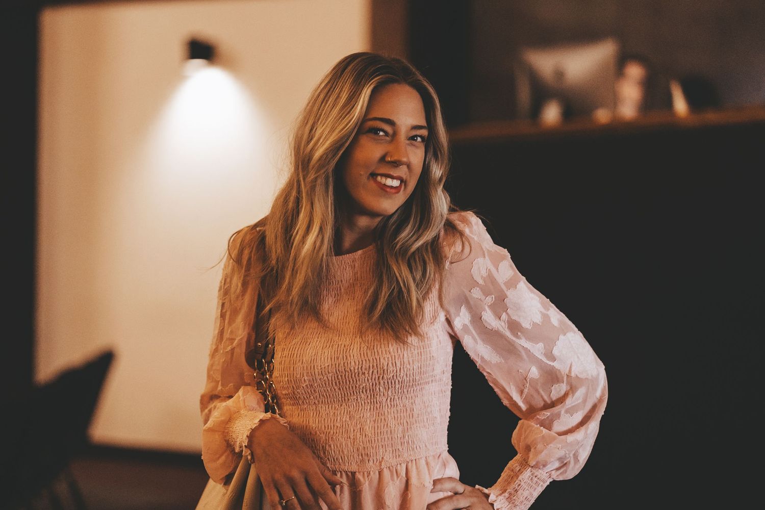 Person wearing pink blouse posing confidently in warm indoor lighting.