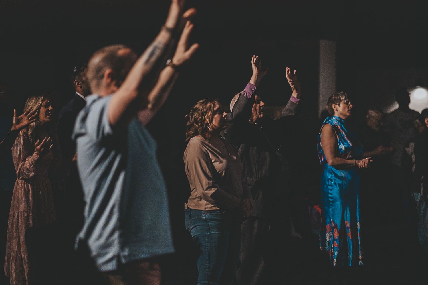 People raising hands in worship during a darkened church service.