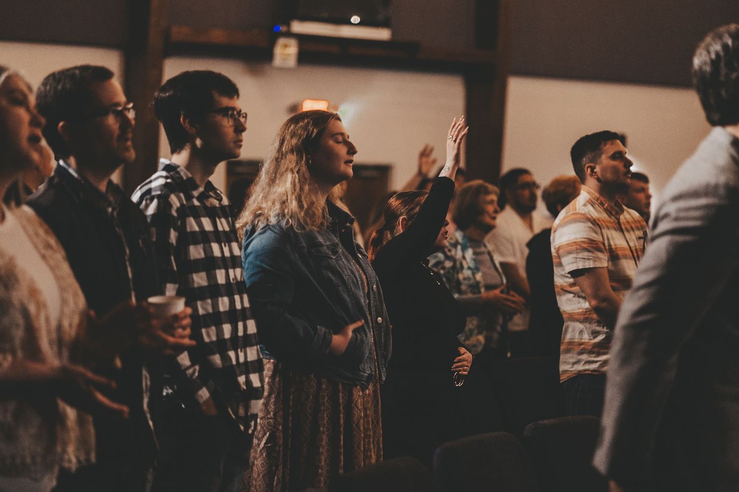 A crowd of people worshipping with raised hands during a church service in dim lighting.