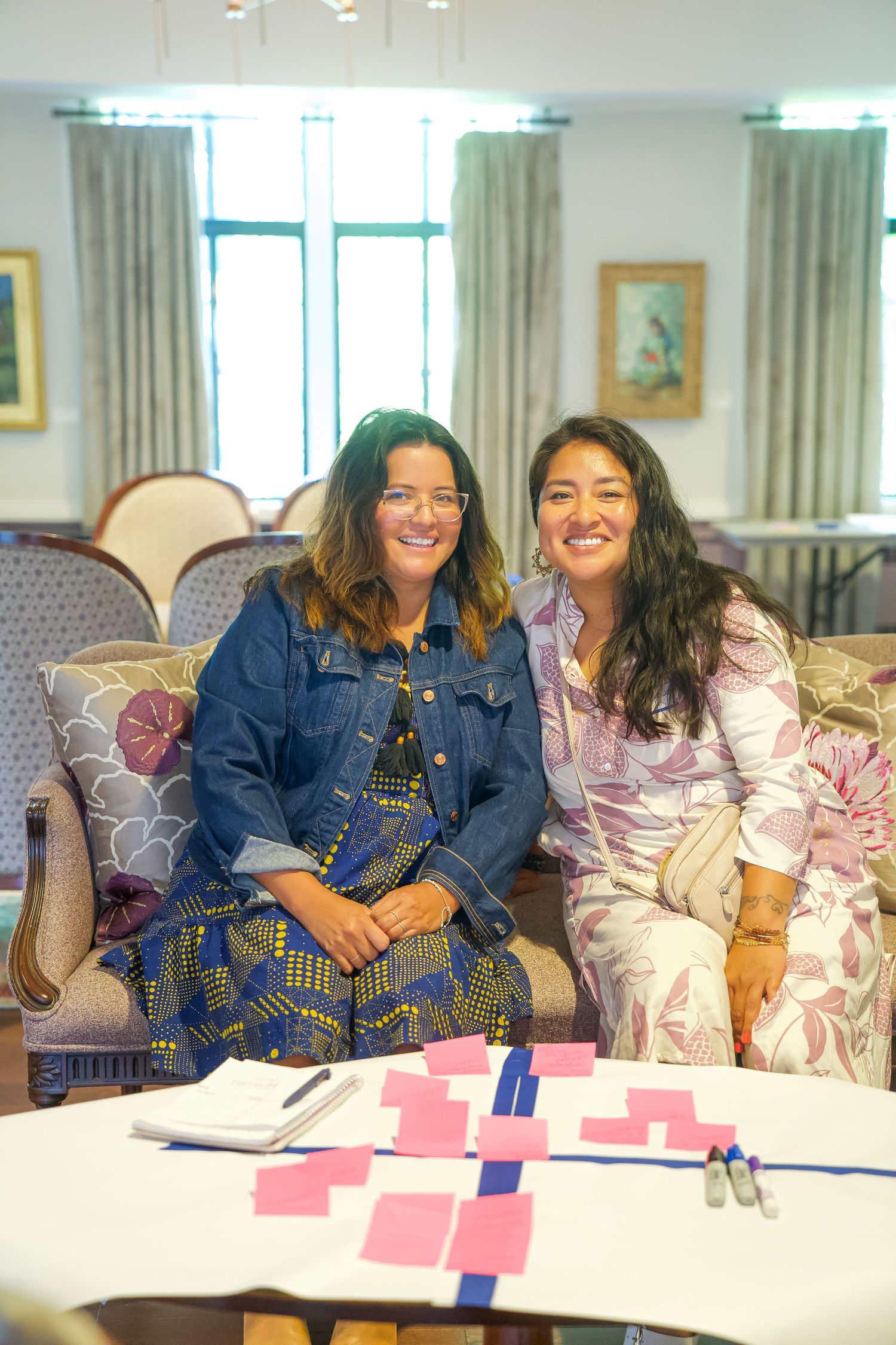 Two people sitting together on a floral couch with playing cards arranged on a table in front of them.