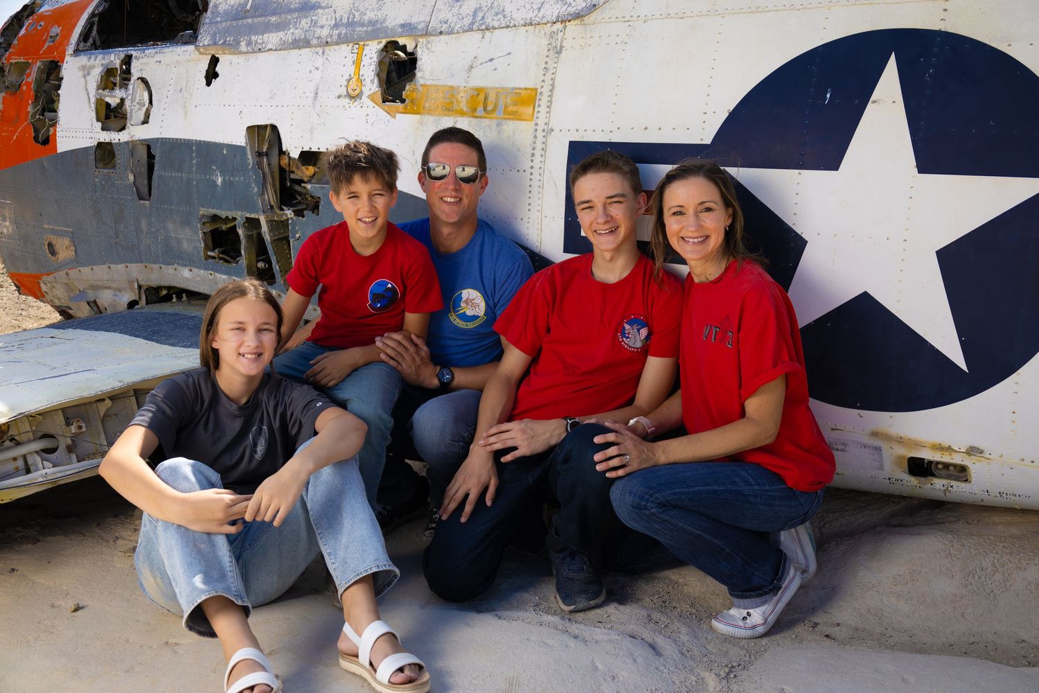 Group photo of people in red shirts sitting by vintage military aircraft.