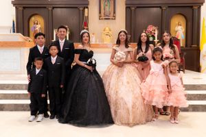 Quinceañera group portrait with celebrants in black and gold gowns surrounded by family in church.