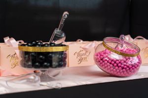 Black and pink candy buffet jars with thank you cards on a white table at a party celebration.