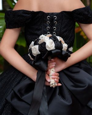 Close-up of quinceañera holding a black and white rose bouquet in a stunning off-shoulder black gown.