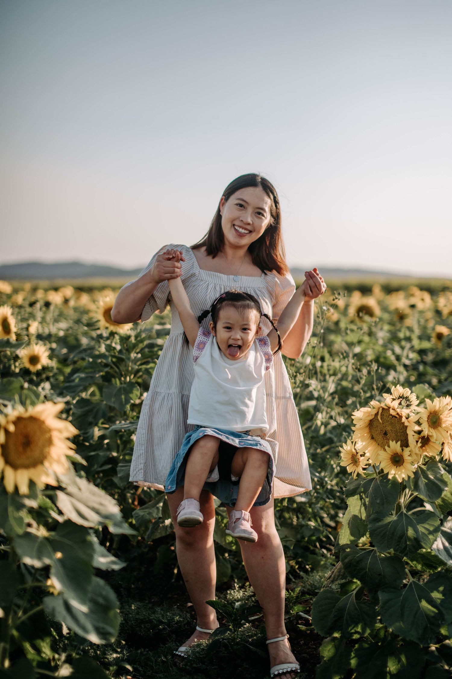 Mother and child playing joyfully among tall sunflowers in evening light.