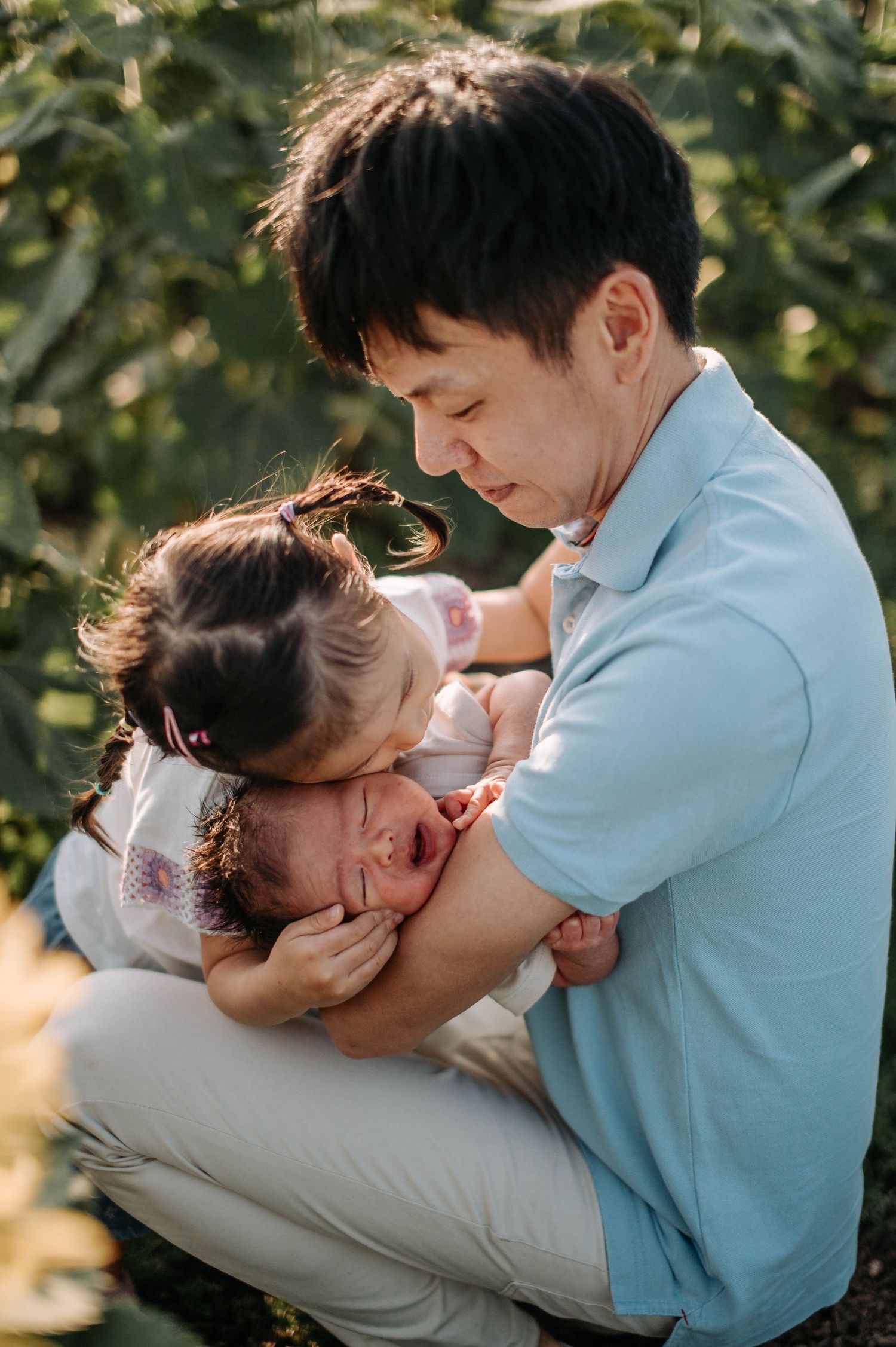 Parent and child share playful cuddles among sunflowers in warm evening light.