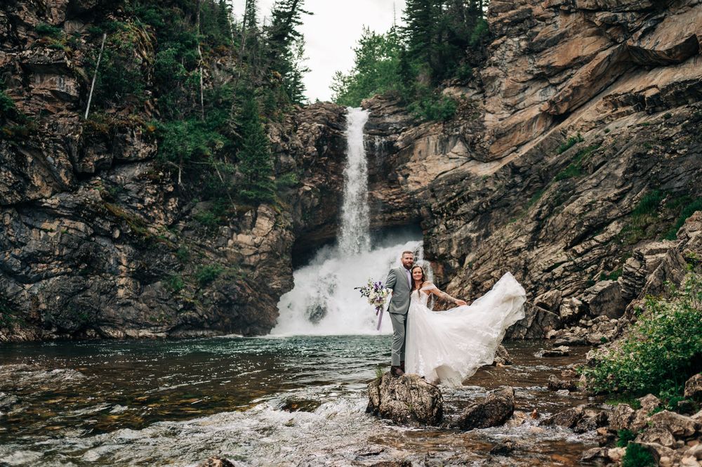 A panoramic view of a cascading waterfall flowing down rocky cliffs surrounded by lush green forest.